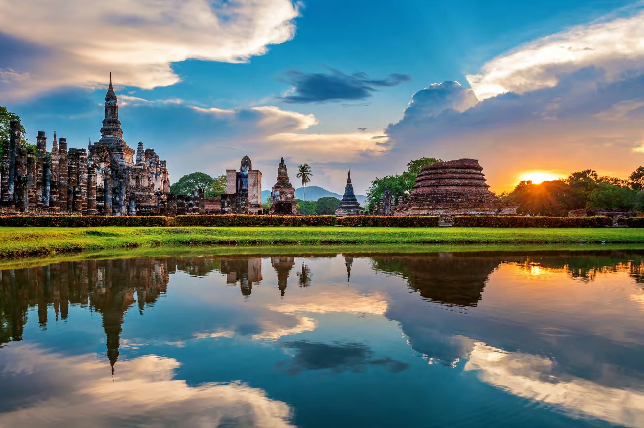 Ruinas de templos del parque histórico de Sukhothai reflejadas en un estanque al atardecer